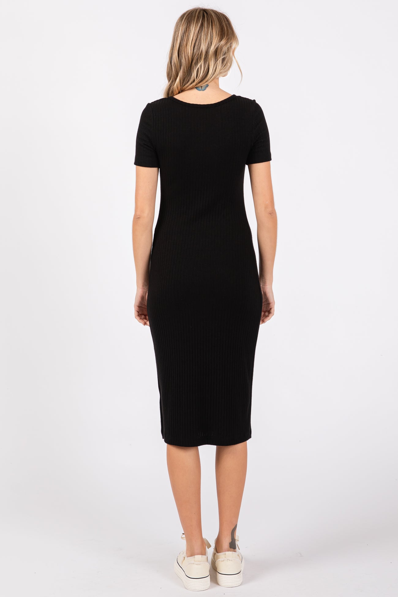 woman wearing a black ribbed midi dress with short sleeves and a fitted silhouette, standing with back to the camera