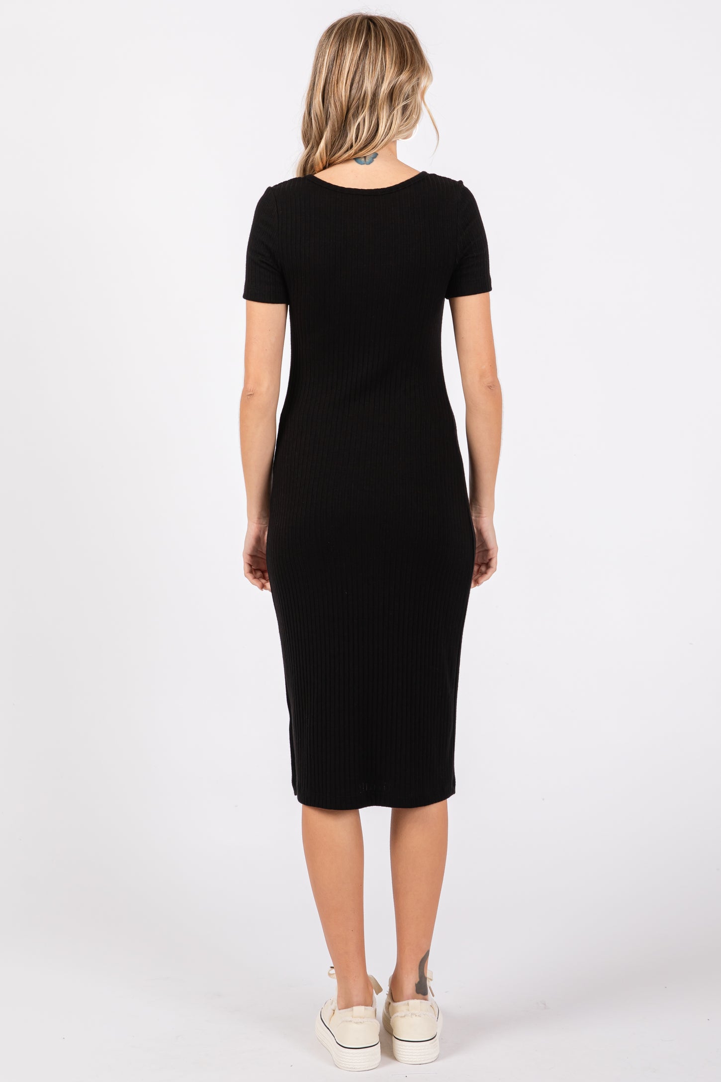 woman wearing a black ribbed midi dress with short sleeves and a fitted silhouette, standing with back to the camera