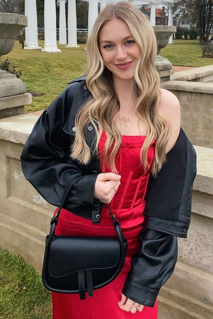 woman wearing a red strapless dress and a black oversized jacket while holding a black handbag