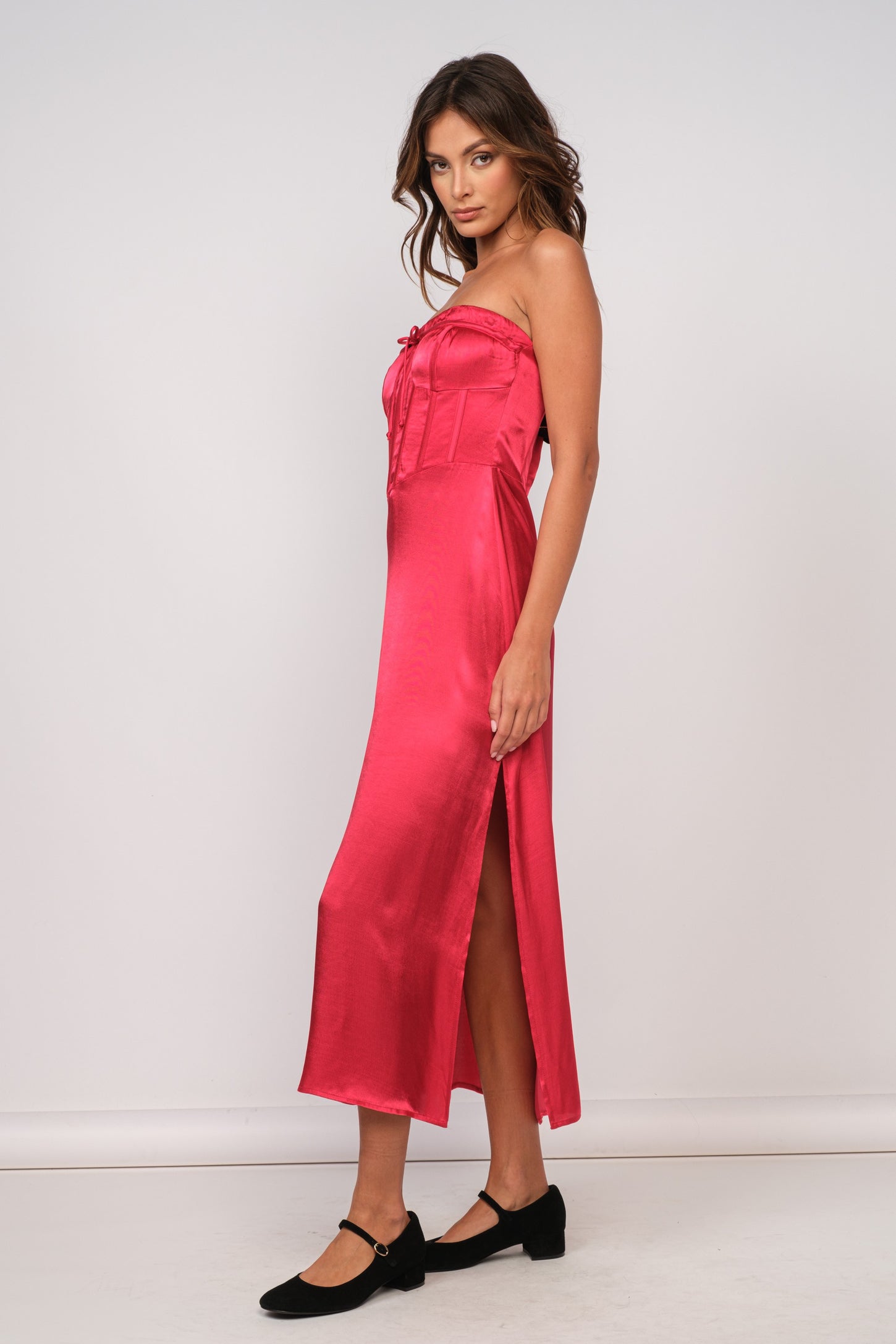 woman wearing a hot pink strapless satin dress with a side slit and tied detail at the bust