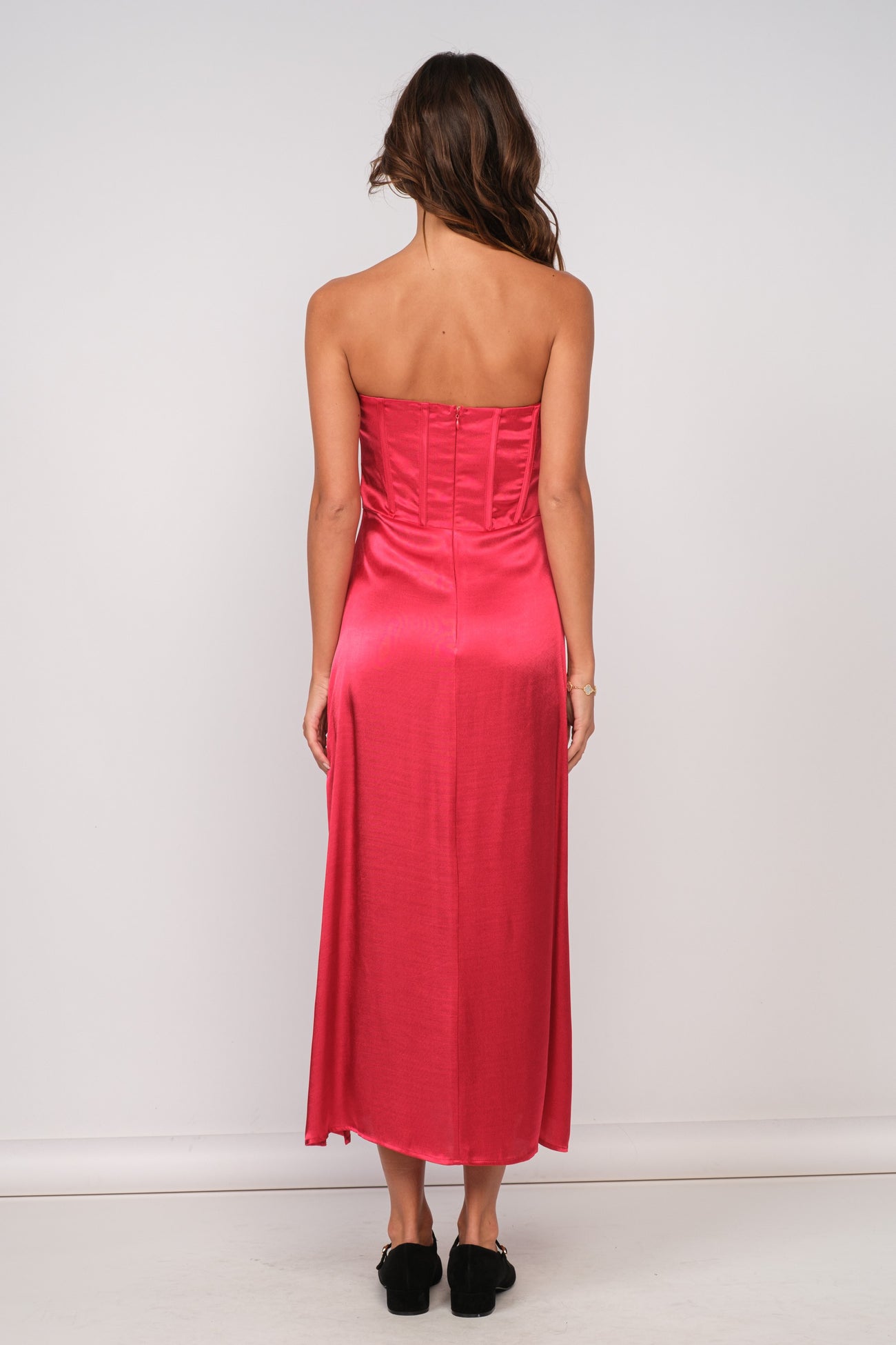 woman wearing a pink strapless satin maxi dress with a fitted bodice and a flowing skirt from the back