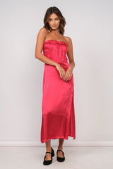 woman wearing a fuchsia satin strapless midi dress with a fitted bodice and side slit, styled with black heels