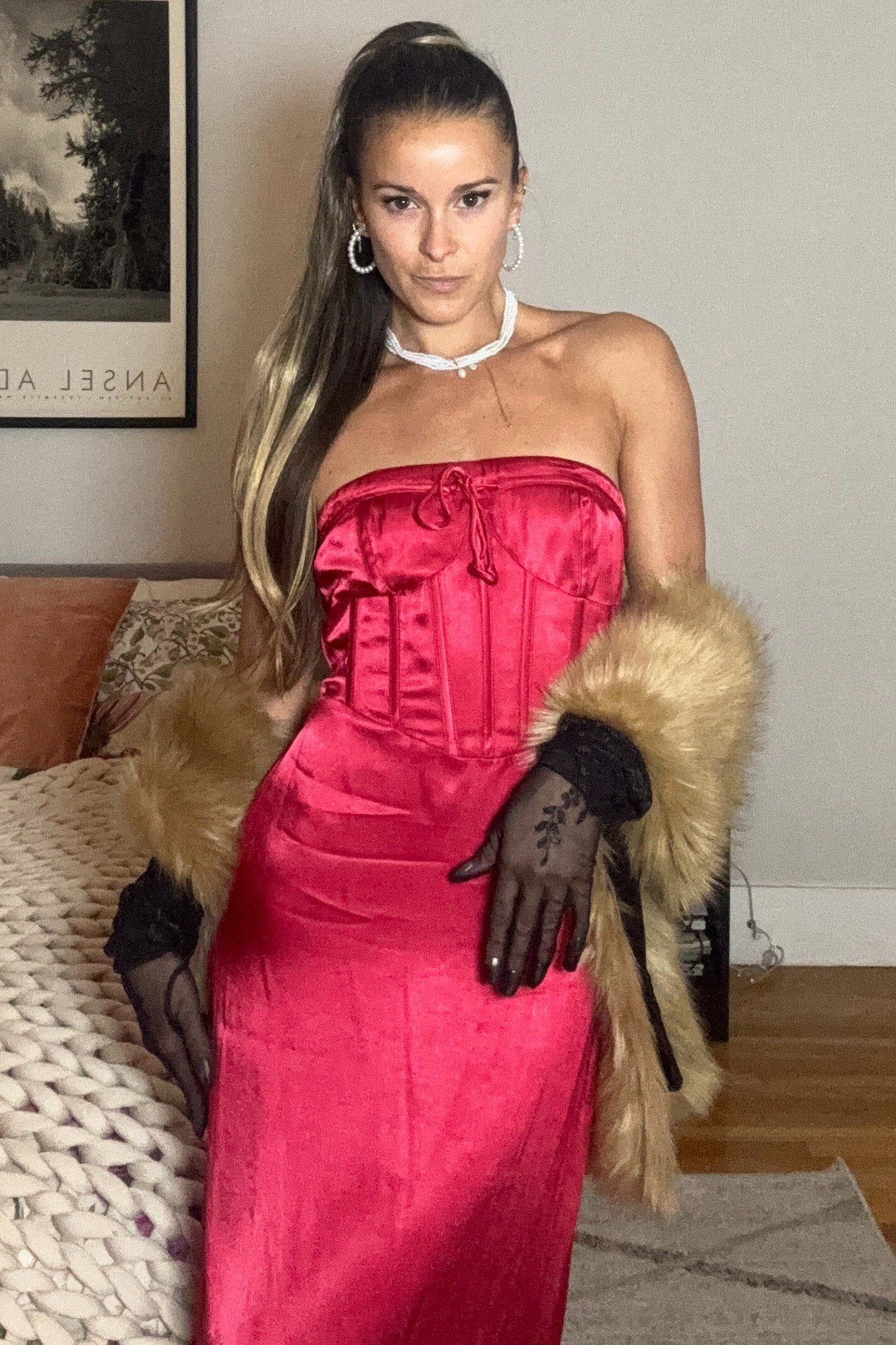 woman wearing a hot pink strapless evening gown with fur cuffs and black gloves, standing in a stylish indoor setting