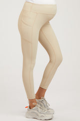 woman wearing light beige maternity leggings with side pockets and a fitted style, showcasing a baby bump