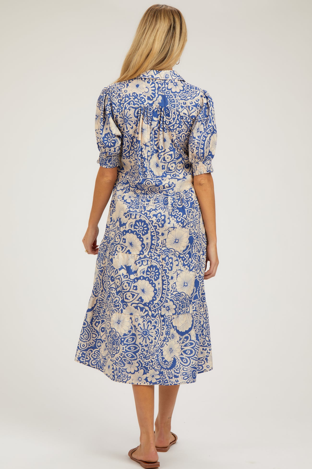 woman wearing a blue and cream floral printed maternity midi dress with puff sleeves and a tie detail at the back