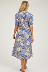woman wearing a blue and cream floral printed maternity midi dress with puff sleeves and a tie detail at the back