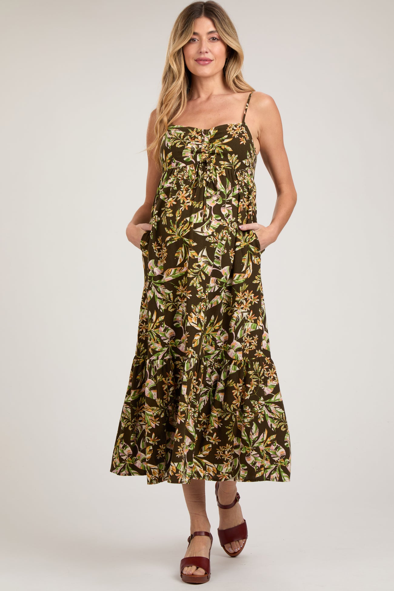 woman wearing a floral maternity maxi dress with pockets and adjustable straps, styled with a flowing hemline