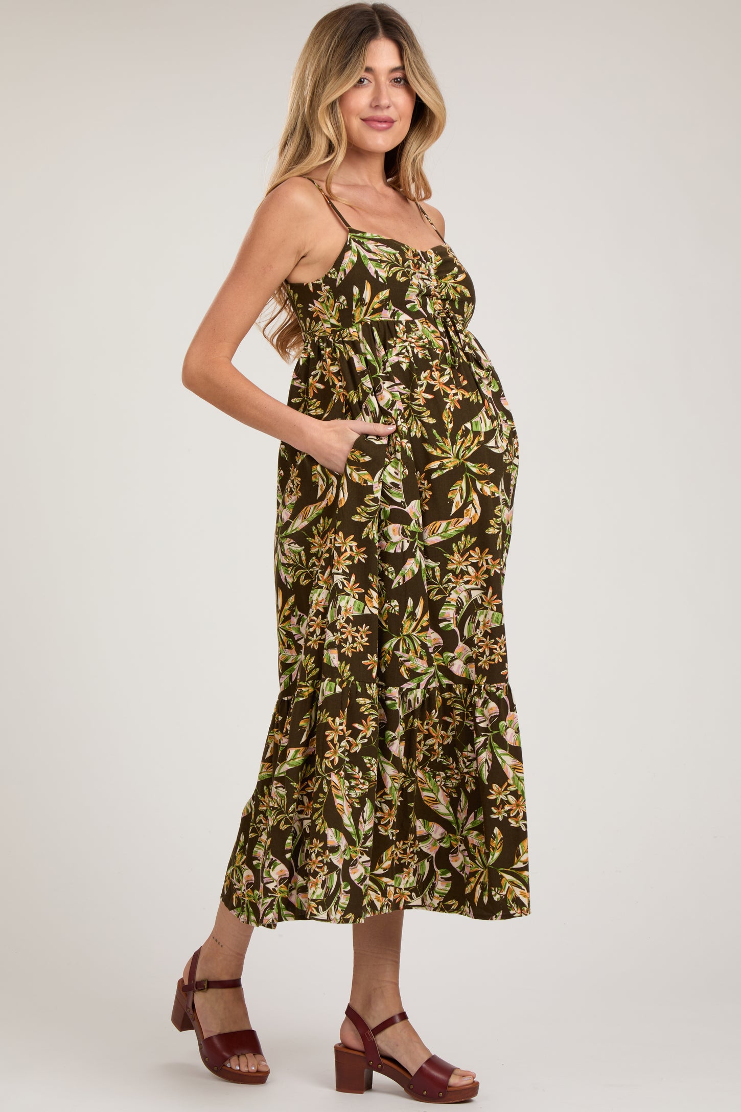 woman wearing a dark floral maternity maxi dress with a baby bump and pockets, standing in strappy brown heels