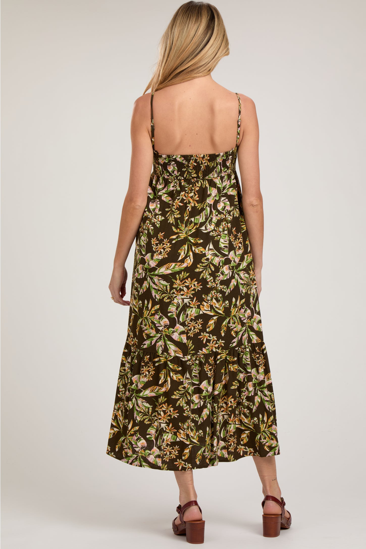 woman wearing a brown floral midi maternity dress with adjustable straps, showing a relaxed fit and tiered design
