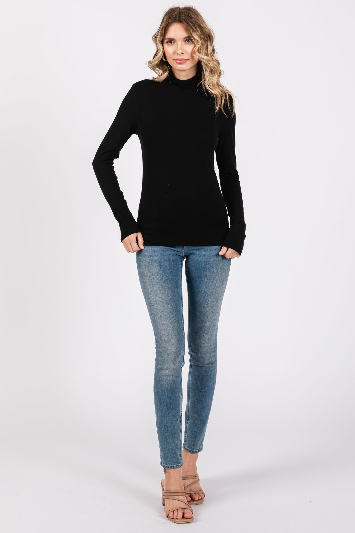 woman wearing a black long sleeve turtleneck top and light blue skinny jeans, standing with hands in pockets