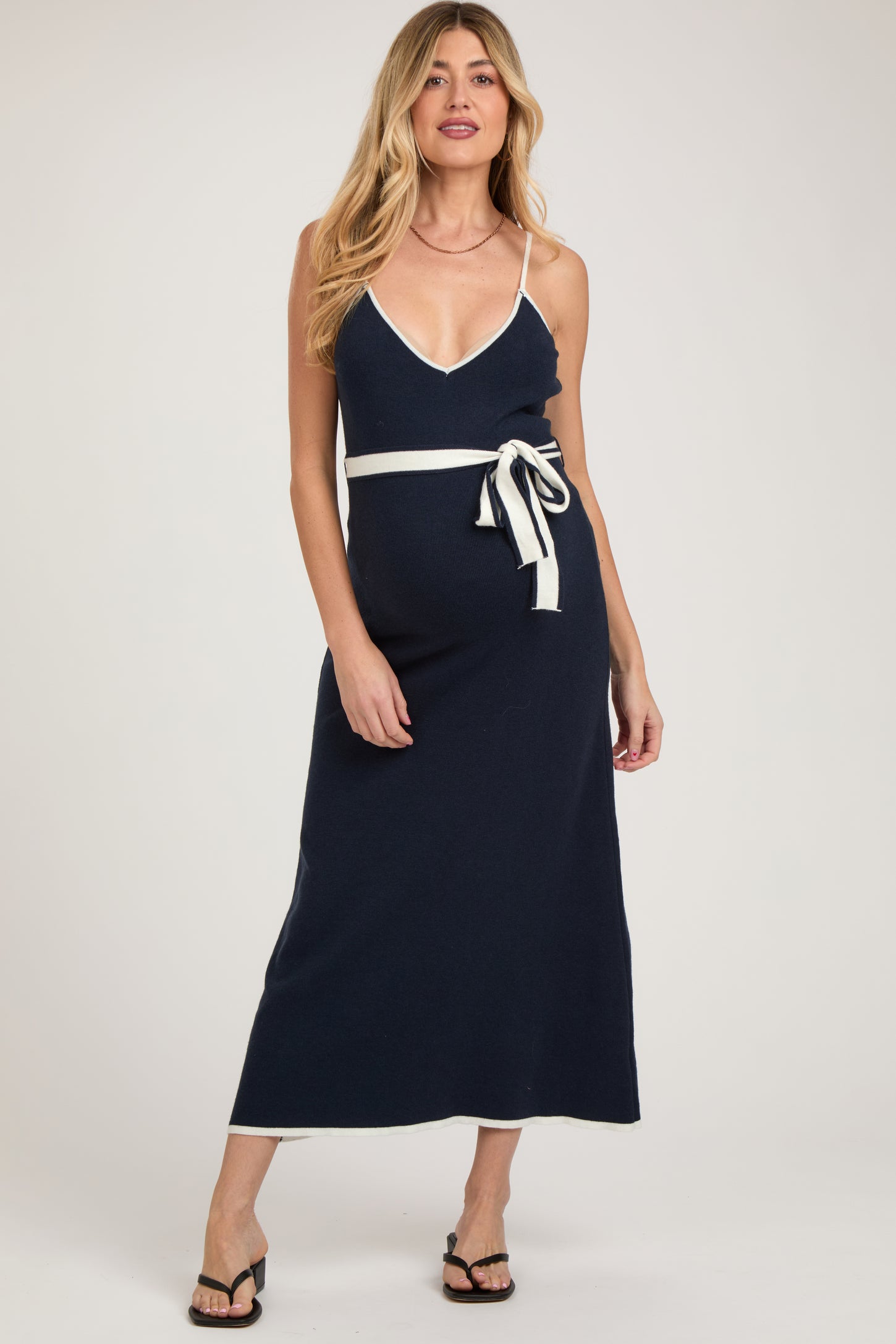 woman wearing a navy blue maternity maxi dress with a v-neck and a white belted waist, showcasing her baby bump