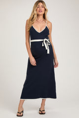 woman wearing a navy blue maternity maxi dress with a v-neck and a white belted waist, showcasing her baby bump