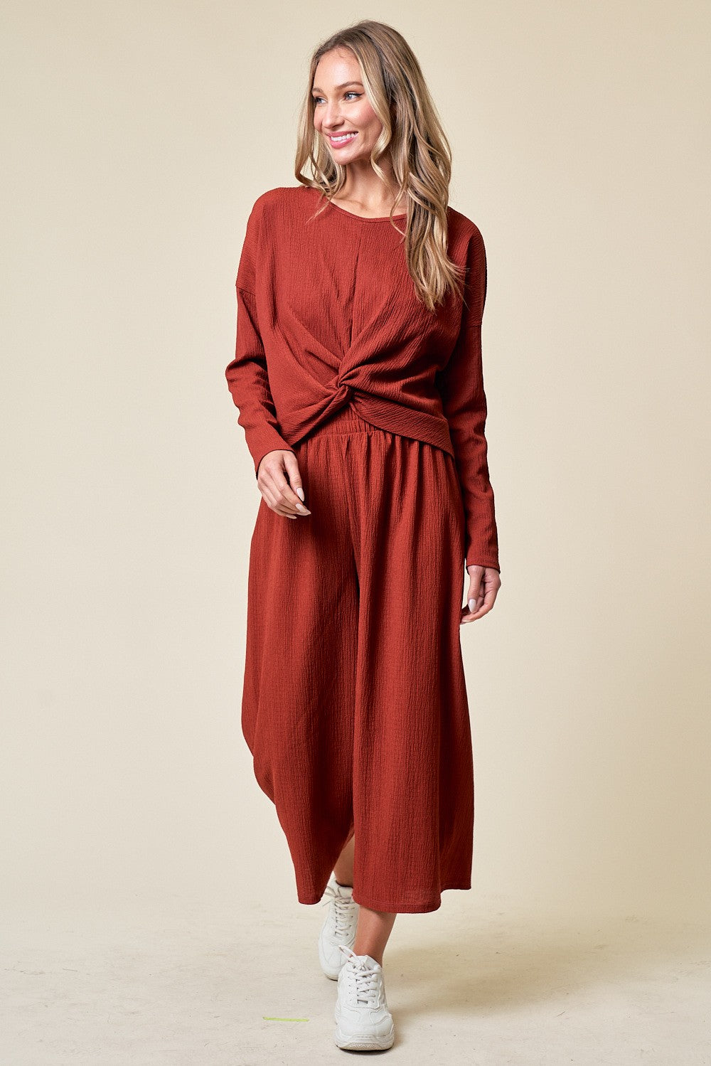 woman wearing a rust-colored long sleeve dress with a knotted front and a flowing midi skirt, paired with white sneakers