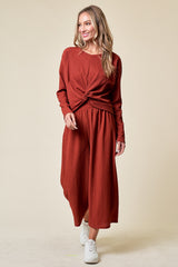 woman wearing a rust-colored long sleeve dress with a knotted front and a flowing midi skirt, paired with white sneakers