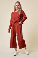 woman wearing a rust-colored long sleeve top with a knotted front and matching wide-leg pants, paired with white sneakers