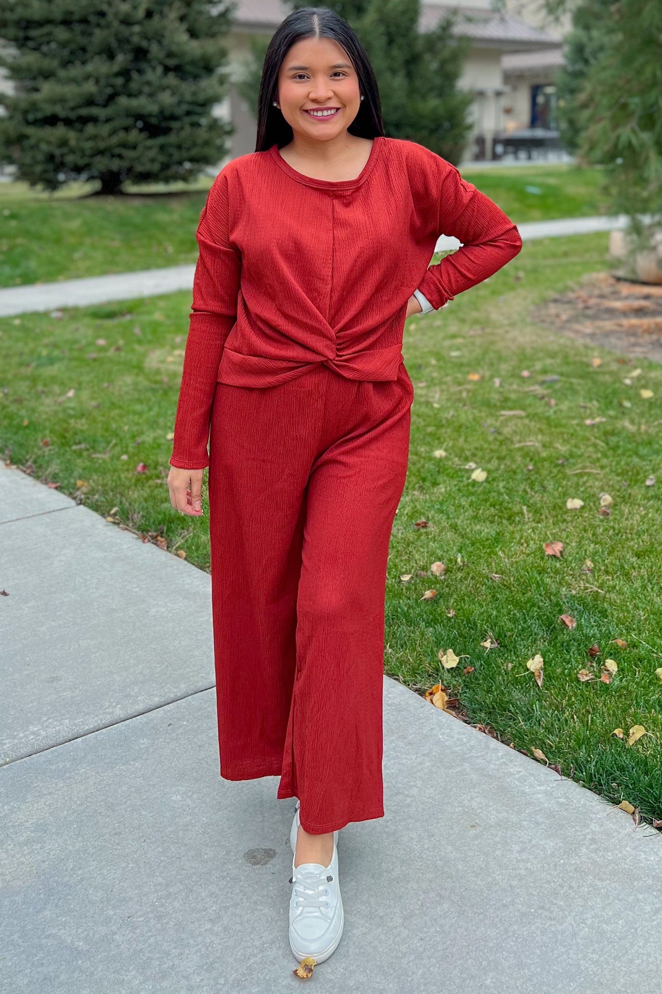 woman wearing a rust-colored long sleeve top with a knot detail and matching wide-leg pants, standing outdoors