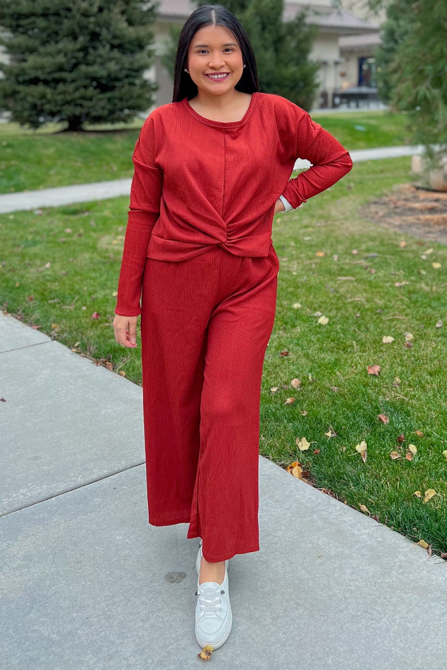 woman wearing a rust-colored long sleeve top with a knot detail and matching wide-leg pants, standing outdoors