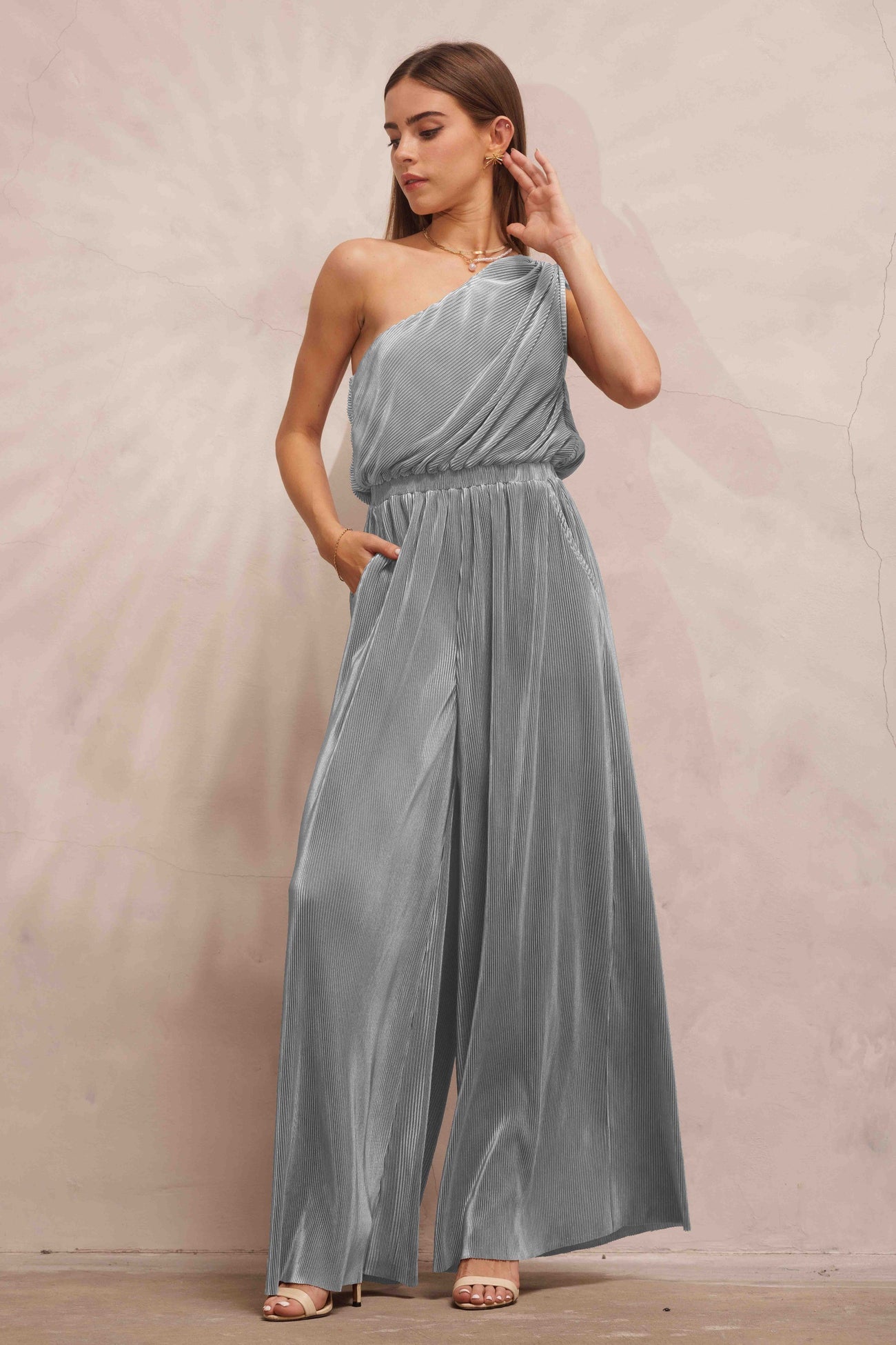woman wearing a silver one-shoulder pleated jumpsuit with wide legs and side pockets