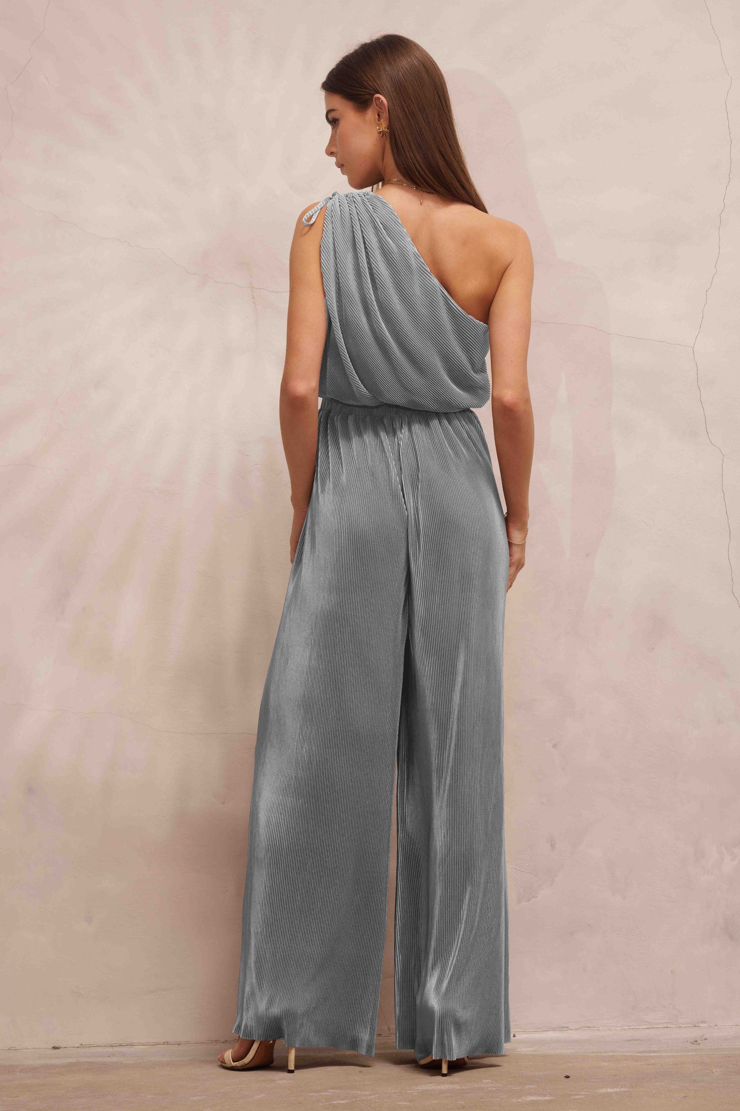 woman wearing a silver one-shoulder jumpsuit with pleated detailing and a wide-leg style