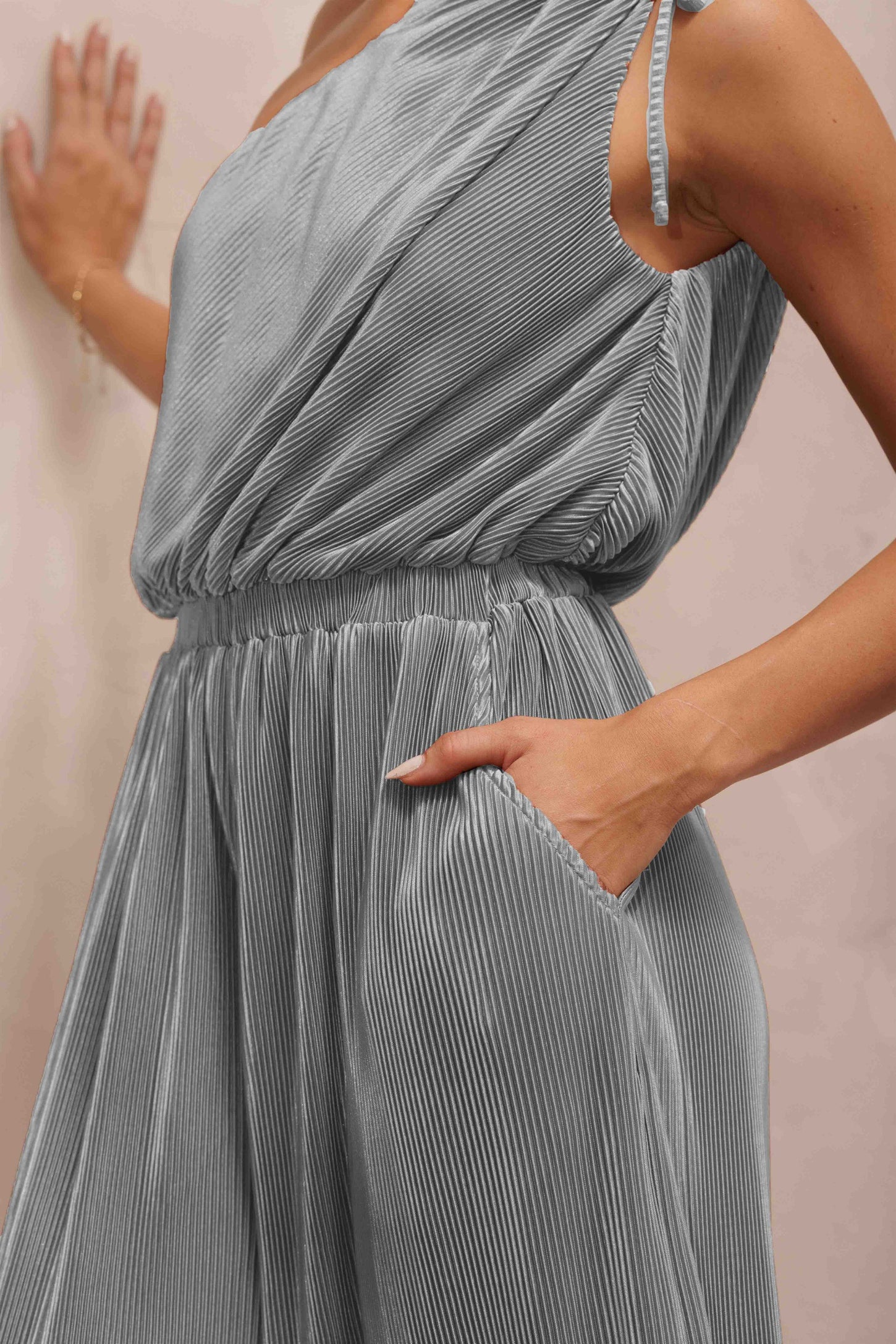 woman wearing a gray pleated sleeveless dress with an elastic waistband and pockets, hand resting on the hip