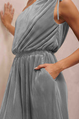 woman wearing a gray pleated sleeveless dress with an elastic waistband and pockets, hand resting on the hip