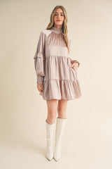 woman wearing a light mauve long sleeve mini dress with ruffle details and high neck, paired with white knee-high boots