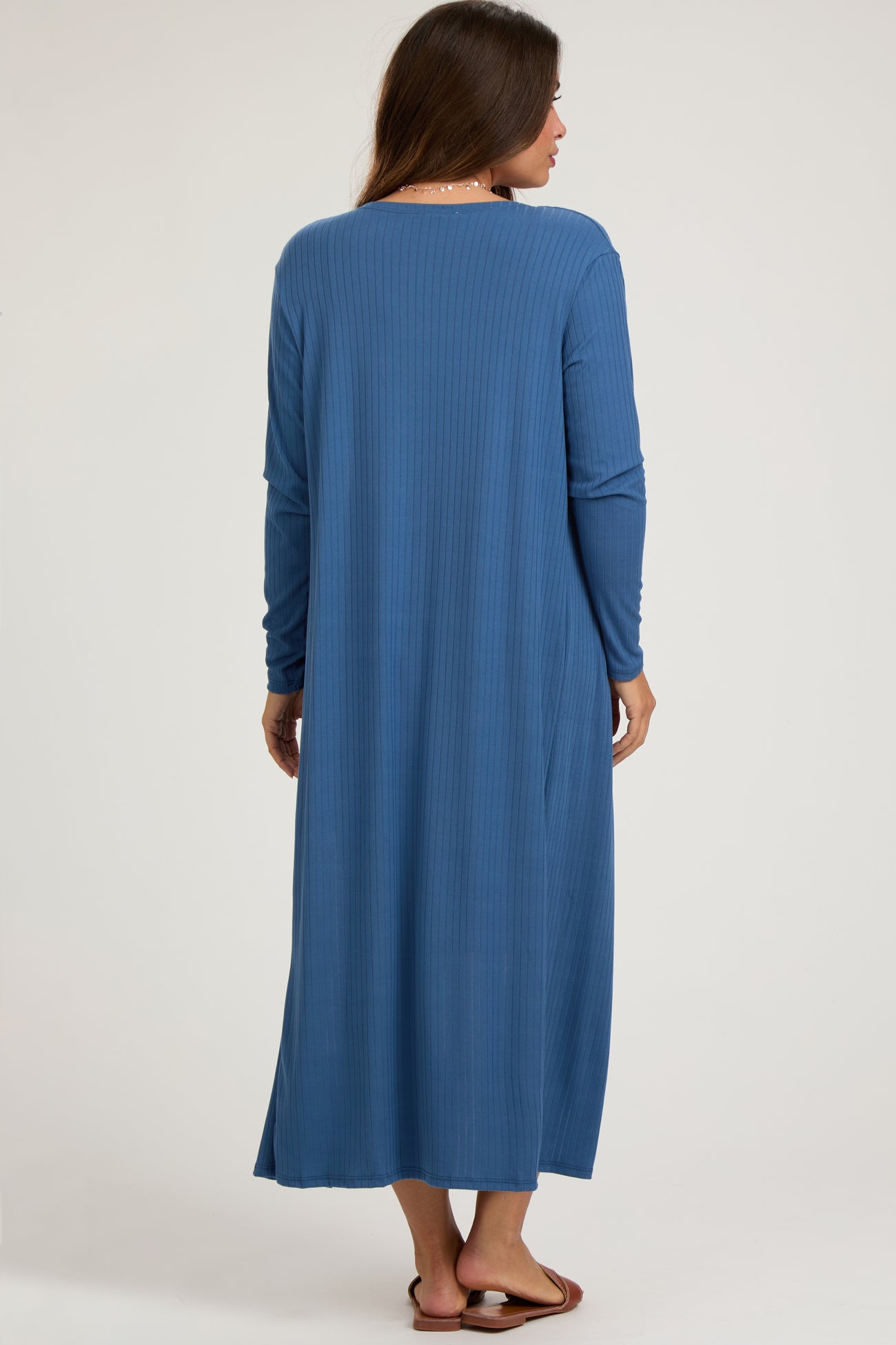 woman wearing a long sleeve blue ribbed maternity dress, shown from the back, with a floor-length silhouette