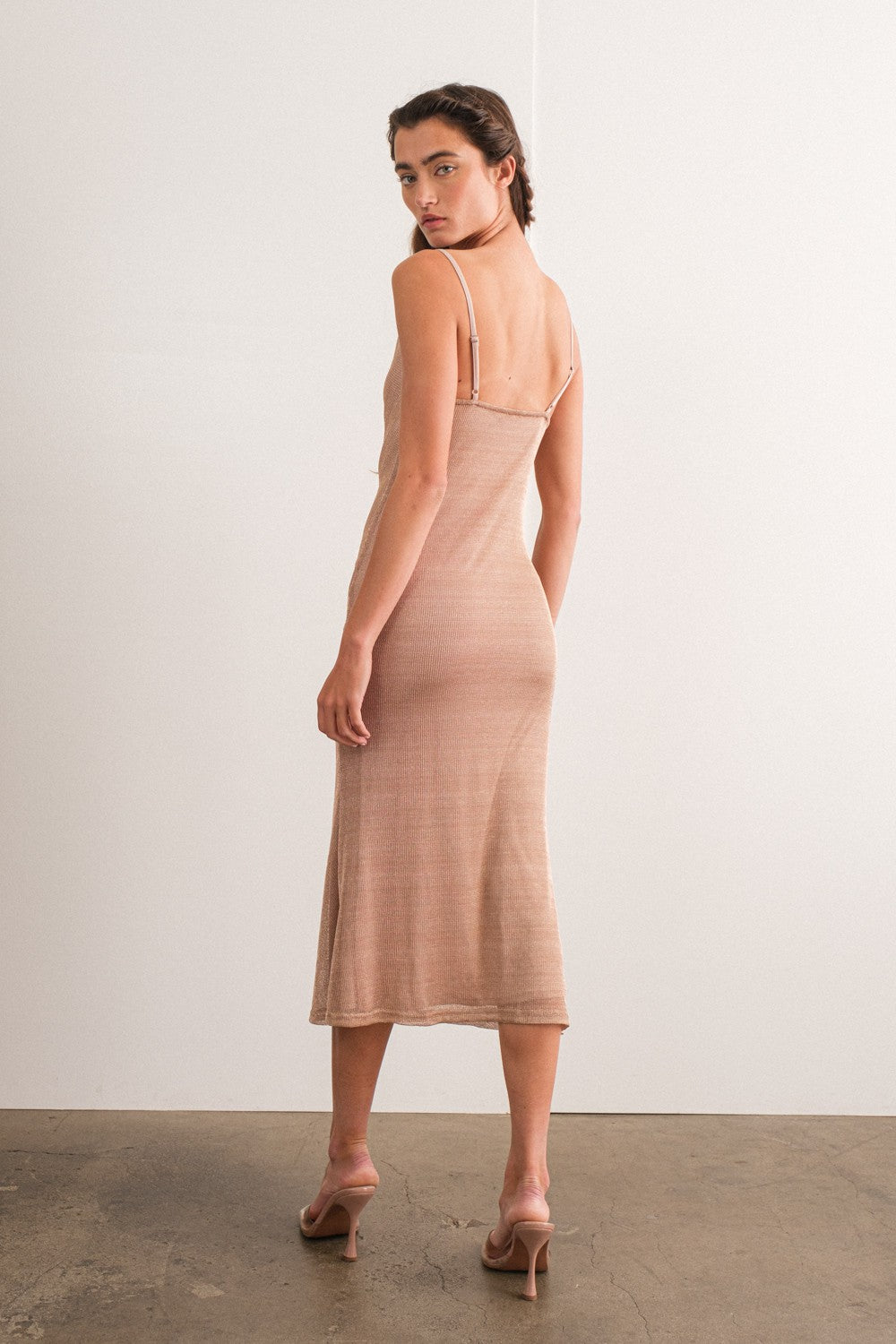 woman wearing a fitted beige ribbed midi dress with thin straps and a back slit, styled with strappy heels