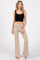woman wearing a black ribbed crop top and beige flared pants, standing barefoot against a white background