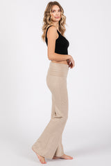 woman wearing a black sleeveless top and beige flared lounge pants, standing sideways with a relaxed pose