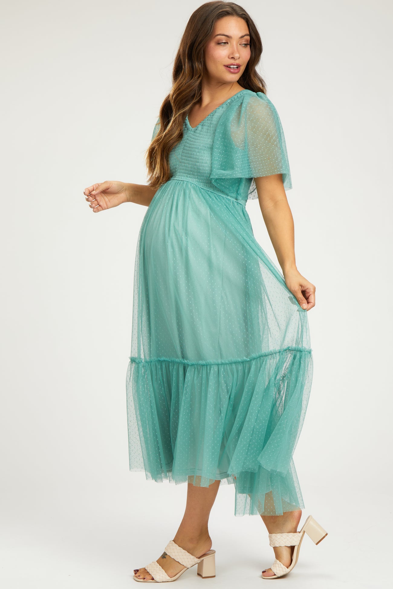 woman wearing a teal maternity dress with a sheer overlay and tiered skirt, showcasing her baby bump