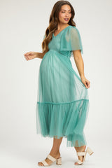 woman wearing a teal maternity dress with a sheer overlay and tiered skirt, showcasing her baby bump