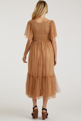 woman wearing a tan maternity dress with a smocked bodice and tiered tulle skirt, displaying a flowy silhouette