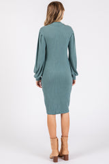 woman wearing a teal ribbed long sleeve midi dress and tan ankle boots, viewed from the back