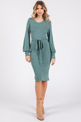 woman wearing a teal long sleeve midi dress with a tied waist and puff sleeves paired with beige ankle boots