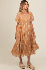 woman wearing a tan maternity dress with floral embroidery and a tiered skirt, styled with wedge sandals