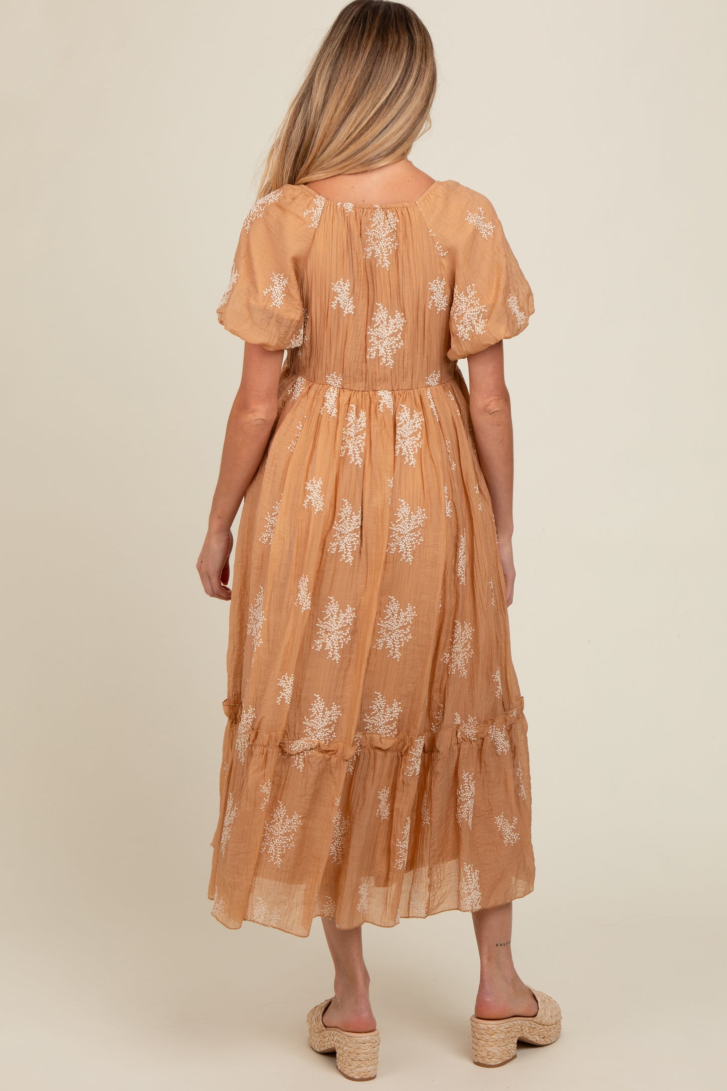woman wearing a light brown maternity maxi dress with floral embroidery and a tiered skirt, showing her baby bump