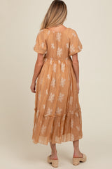 woman wearing a light brown maternity maxi dress with floral embroidery and a tiered skirt, showing her baby bump
