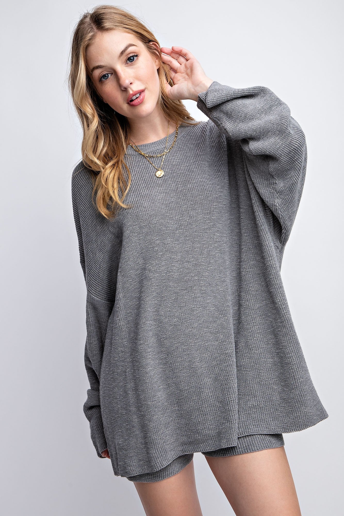 woman wearing a gray oversized knit sweater with long sleeves and a relaxed fit, styled with layered gold necklaces