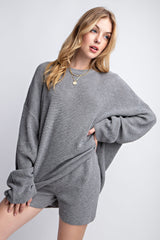 woman wearing a gray oversized ribbed sweater with long cuffs and styled with casual shorts