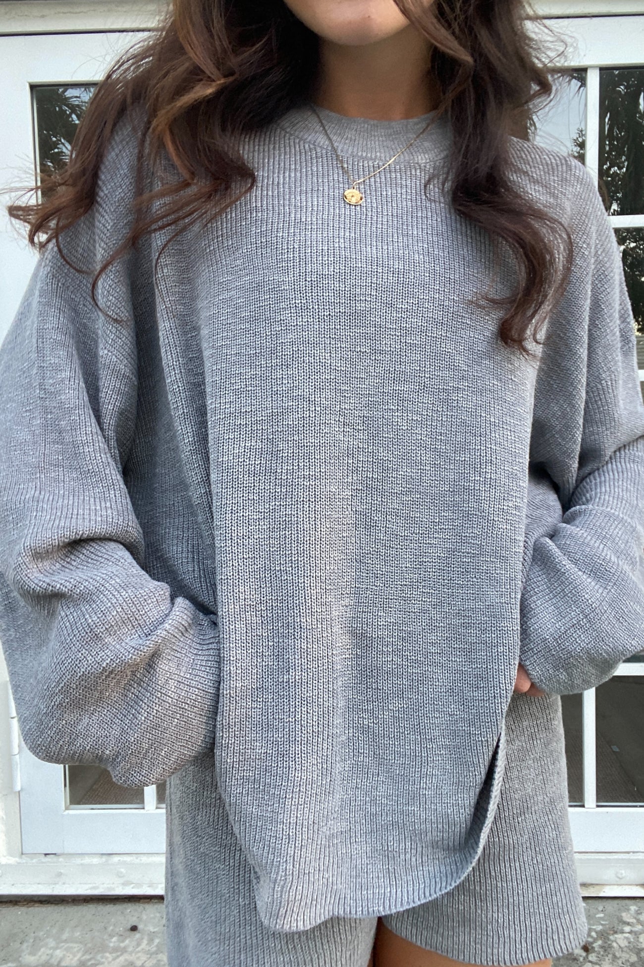 woman wearing an oversized gray knit sweater with long sleeves and a relaxed fit, hands in pockets