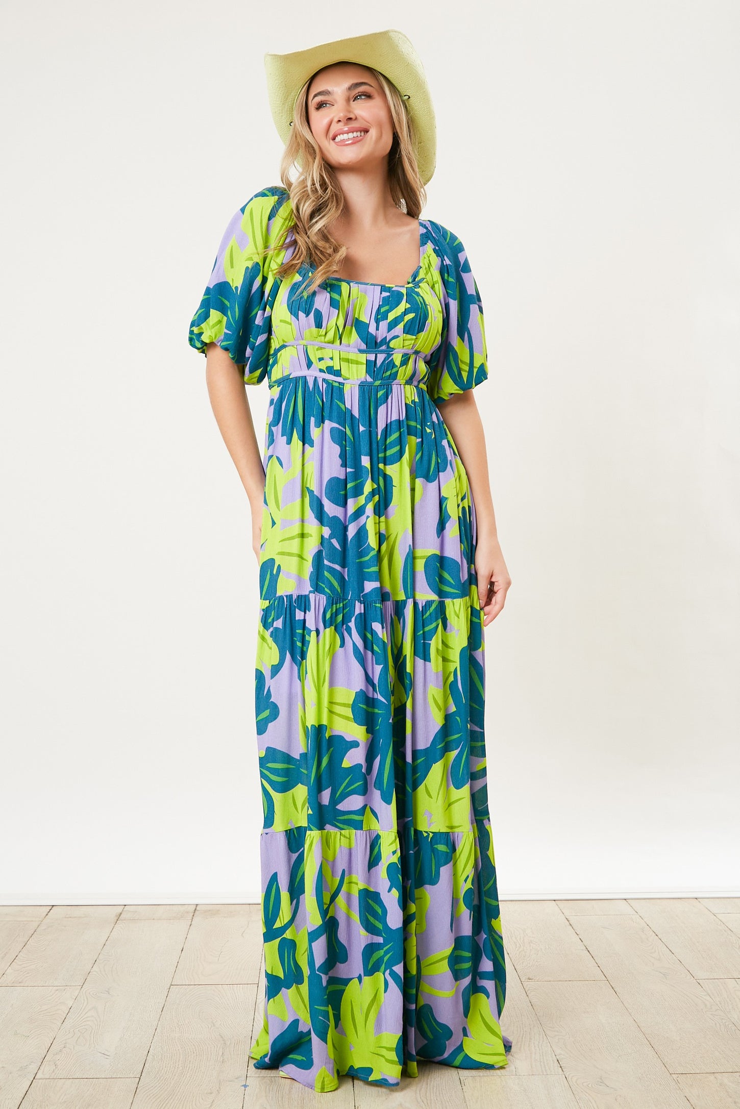 woman wearing a purple and green floral maxi dress with puff sleeves and a cinched waist, accessorized with a cowboy hat