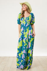 woman wearing a colorful green and blue floral maxi dress with puff sleeves and a square neckline, accessorized with a wide-brimmed hat