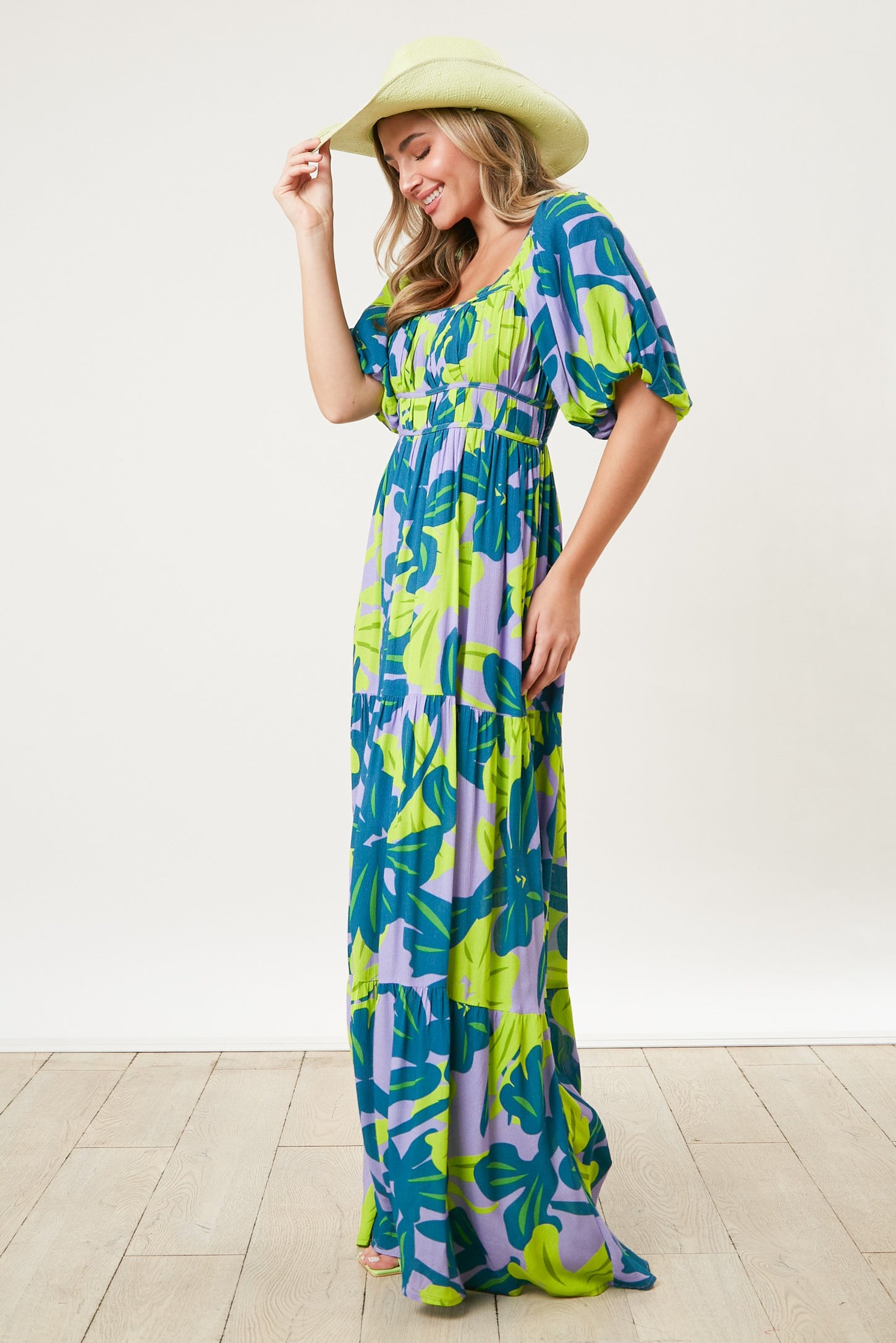 woman wearing a colorful floral maxi dress with puff sleeves and a fitted bodice, holding a straw hat