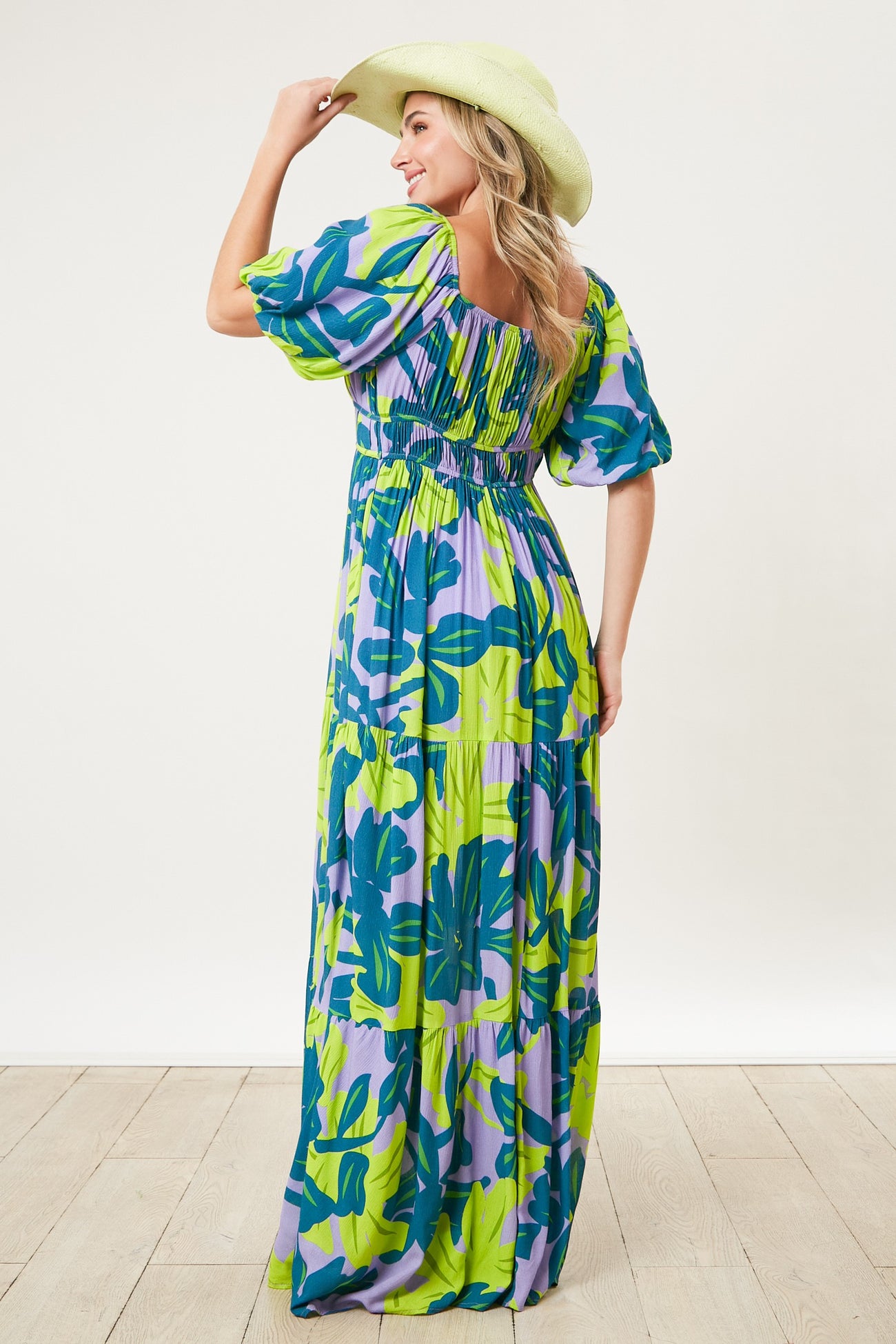 woman wearing a colorful floral maxi dress with puff sleeves and a smocked back, holding a wide-brimmed hat