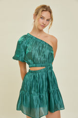 woman wearing a green one-shoulder dress with a cut-out waist and tiered skirt