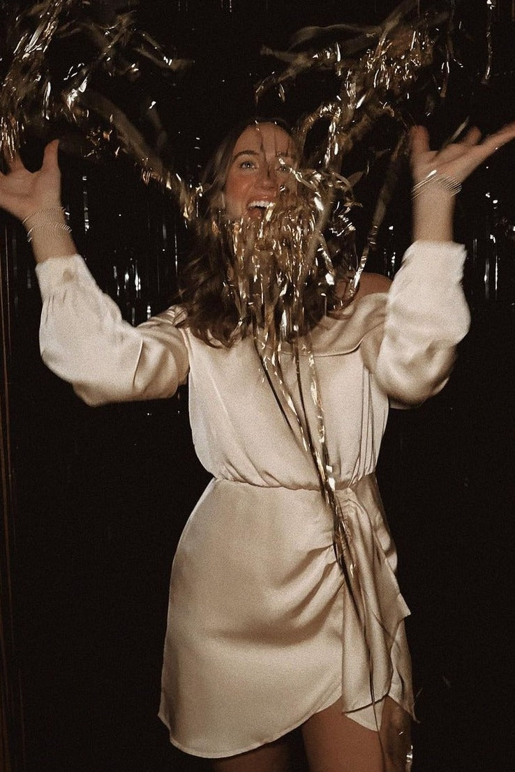 woman wearing a light pink off-shoulder mini dress and holding gold streamers in celebration