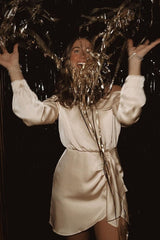 woman wearing a light pink off-shoulder mini dress and holding gold streamers in celebration