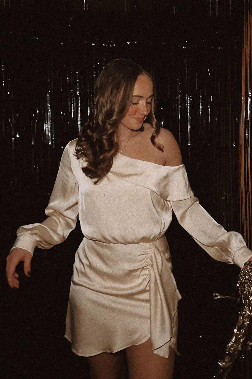 woman wearing a champagne off-the-shoulder satin dress with long sleeves and a wrap detail at the waist