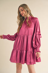 woman wearing a pink tiered mini dress with long sleeves and smocked detailing on the neckline and cuffs